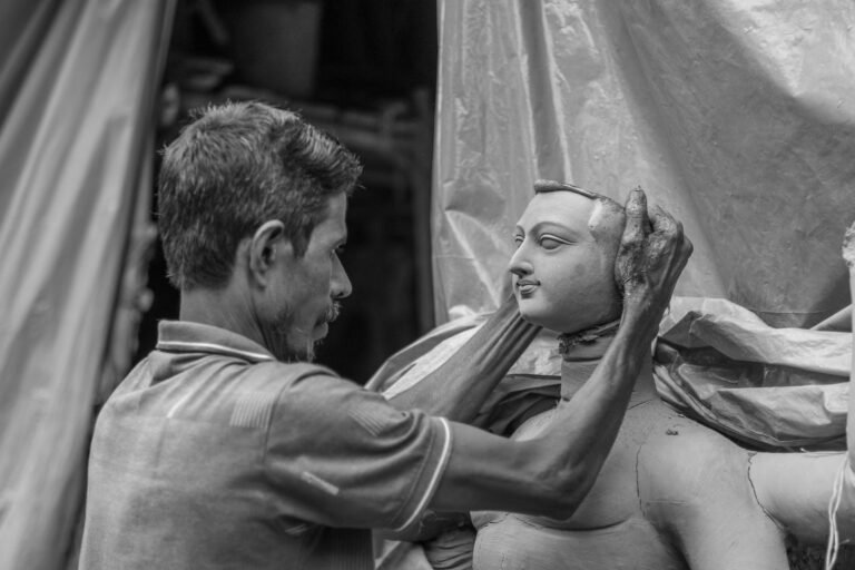 A craftsman shaping the face of a clay statue, in black and white